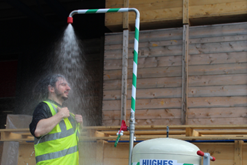 Worker in high vis standing under an activated Hughes mobile safety shower